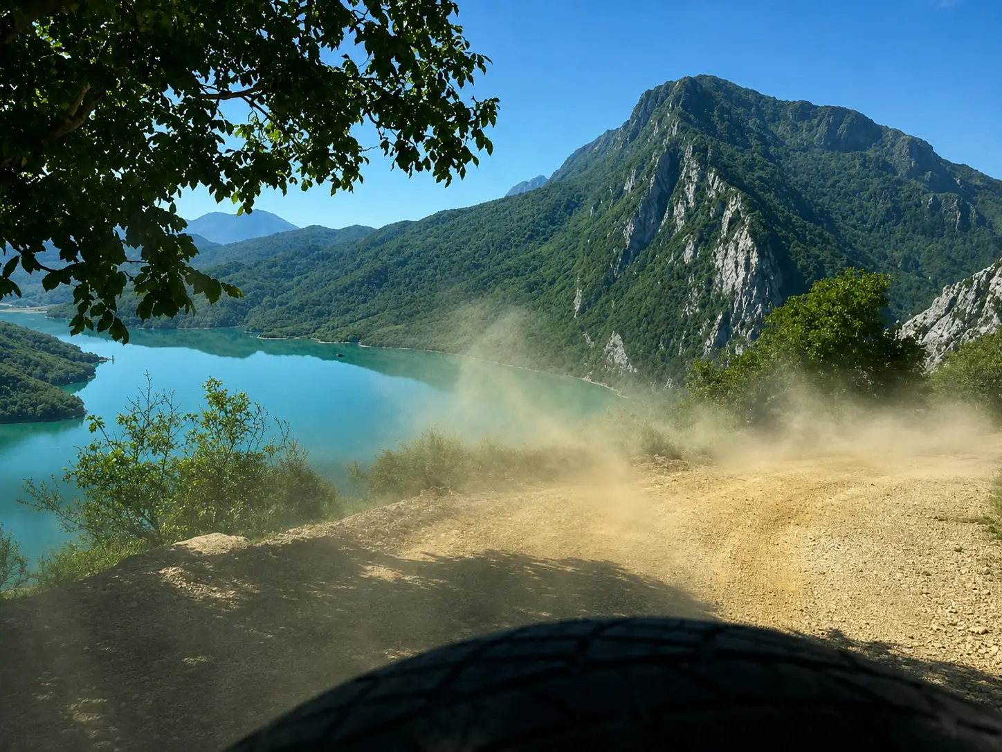 The view forward from the 4×4 on the dusty gravel track, dust hanging in the air above the turquoise water with the limestone ridge beyond.