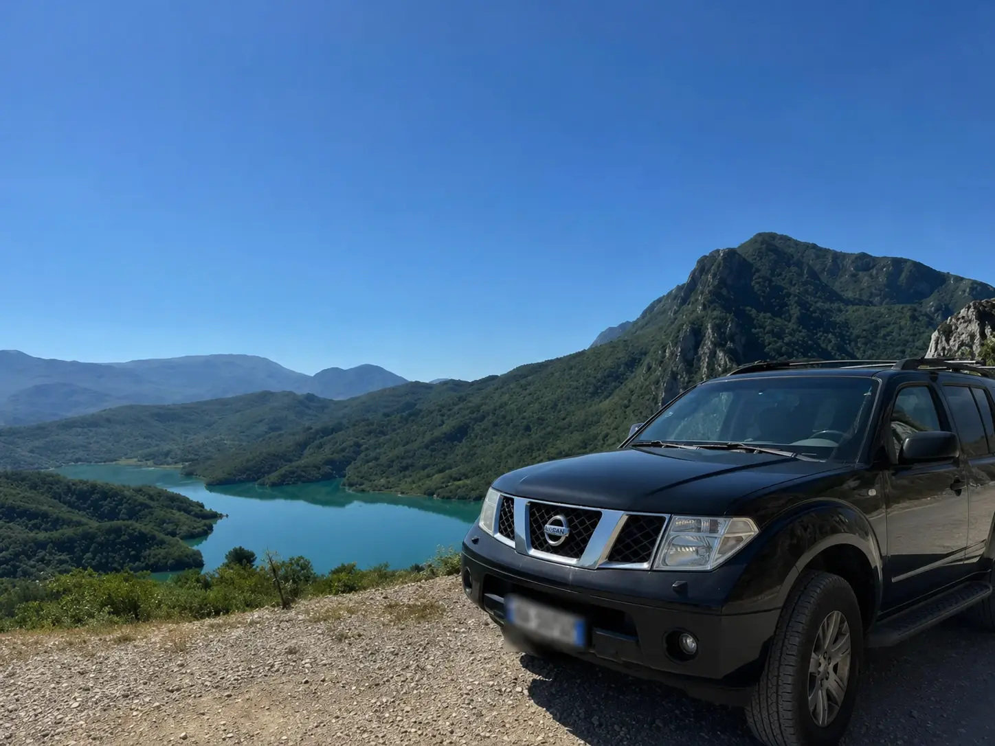 The tour's black Nissan Pathfinder at a gravel pull-off high above Lake Bovilla, the reservoir winding between the ridges below.