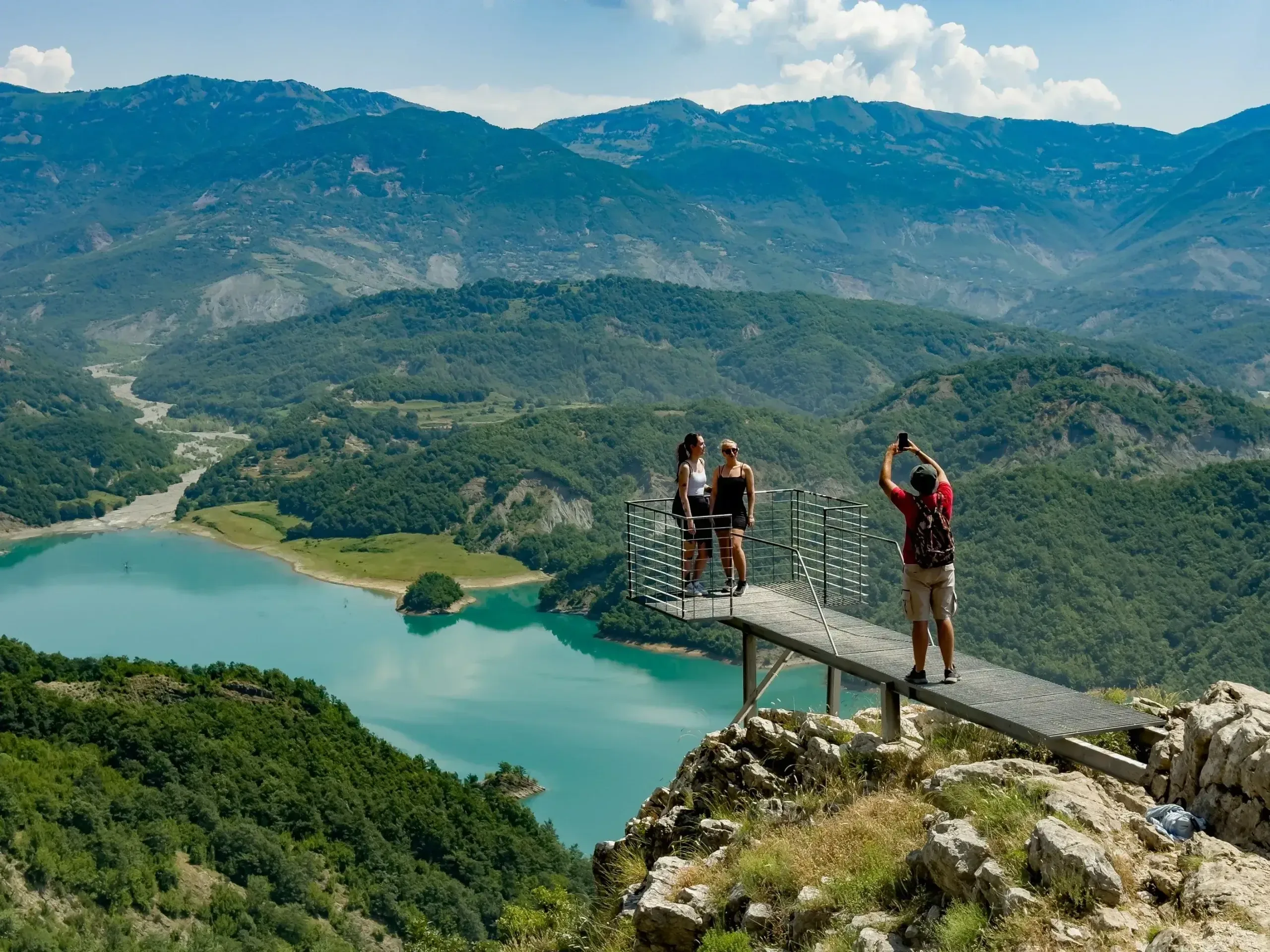 Visitors on the Balcony of Bovilla viewing platform, with Lake Bovilla's turquoise water and the Dajti mountain range stretching behind them.