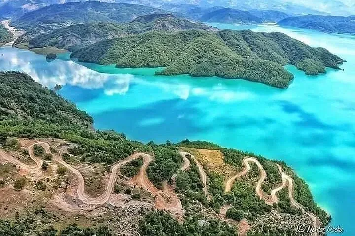 Aerial view of the switchback mountain road leading down to the turquoise waters of Lake Bovilla — the dirt track only 4×4 vehicles handle comfortably.