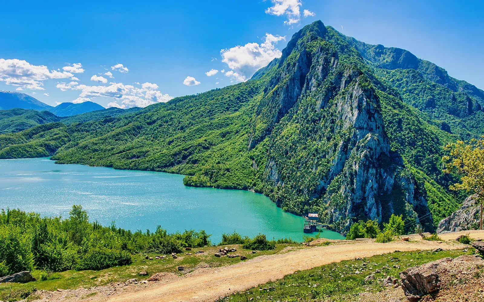 Turquoise waters of Lake Bovilla reservoir framed by green hills and the Dajti National Park ridge line.